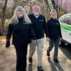 two women and a man are walking beside a merry maids car wearing black merry maids tops